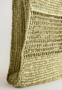 Borsa a rete intrecciata di colore verde chiaro, realizzata in materiale simile a paglia, presenta un design a rete aperta testurizzato con bordi rinforzati per maggiore robustezza.