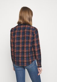 Camicia di flanella a quadri blu navy e arancione con maniche lunghe, orlo arrotondato e colletto standard. Tessuto morbido con motivo a scacchi.