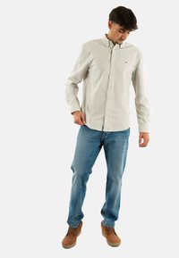 Camicia button-up a righe grigio chiaro con colletto, abbinata a jeans blu chiaro e stivali marroni, con un design semplice e vestibilità standard.