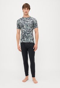 Kortærmet, tætsiddende skjorte i et grønt camouflage mønster, parret med sorte, slim-fit bukser, begge lavet af strækbart stof.