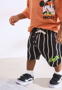 Black and cream striped shorts with green embroidery, paired with a peach t-shirt featuring a character graphic, and black sneakers with white soles.