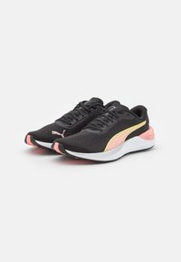 Zapatillas deportivas negras con un upper de tela texturizada, acentos en rosa y amarillo neón, y una suela blanca acolchada. Presenta un logo prominente.
