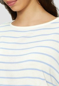 Haut en tissu tricoté blanc avec des rayures horizontales bleues, présentant un col rond et une coupe décontractée. Texture douce, montrant une légère élasticité.