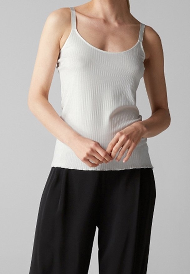 Top de tirantes finos blanco acanalado con escote en forma de barco, combinado con unos pantalones negros holgados, que muestran una silueta ajustada y una textura suave.