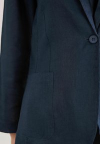 Marinblå linblazer med rabatterad krage, enkel knappstängning och framficka med slät textur.
