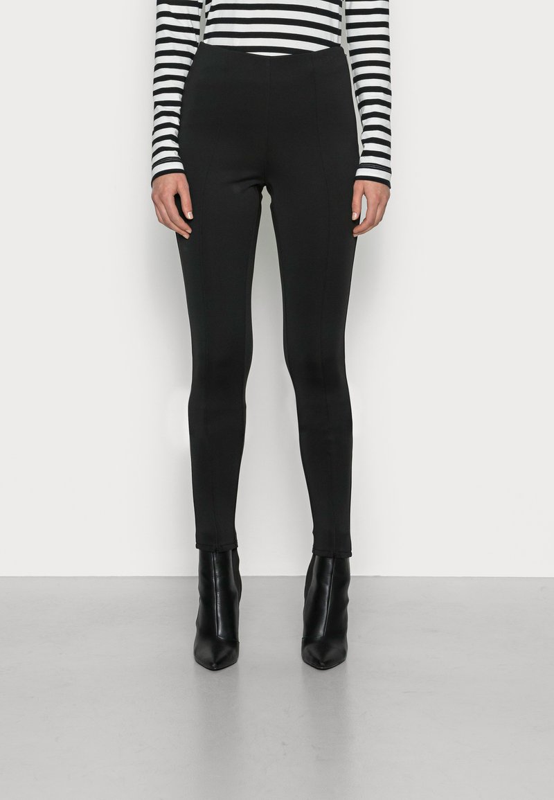 Pantaloni neri a vita alta con una vestibilità slim, caratterizzati da una trama liscia e linee pulite, abbinati a stivaletti neri lucidi con punta affusolata.