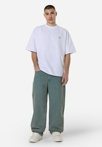 White oversized t-shirt with a small logo, paired with light blue baggy jeans and white sneakers, featuring a relaxed fit and soft texture.