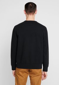 Felpa nera con maniche lunghe, collo rotondo e polsini a costine. Realizzata in morbido cotone, presenta un design pulito e minimalista senza grafiche.
