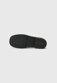 Suola di scarpa in gomma nera con un design testurizzato, caratterizzata da un motivo a zigzag e un tacco piatto per stabilità.