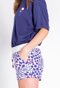 Marineblauw kortemouwen shirt met florale borduursels; witte shorts met een kleurrijk luipaardmotief en zijzakken.