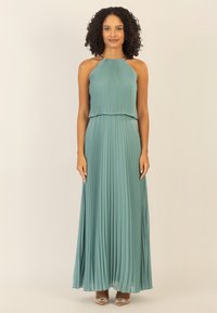 Langes, gepliesstes Kleid in Petrol mit einem Halterneck und bestickten Akzenten. Fließender Stoff, der bis zum Boden reicht, ergänzt durch Riemchensandalen.