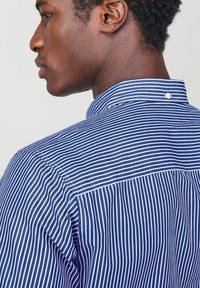 Blauw-wit gestreepte shirt met een verhoogde kraag, voorzien van een knoopdetail aan de achterkant. Glad stof met een getailleerde pasvorm en nauwkeurige stiksels.