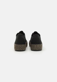 Scarpe slip-on nere in tela con suole texturizzate intrecciate e tacchi piatti, caratterizzate da una finitura liscia e un design minimalista.