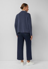 Marineblaues, übergroßes Sweatshirt mit Kragen, kombiniert mit weit geschnittenen Jeans und weißen Sneakers. Strukturierter Stoff mit lockerer Passform.