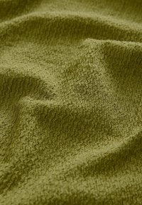 Texturerad tyg i mossgrön, med ett vågigt mönster. Materialet har ett mjukt utseende med subtil djup och dimension.