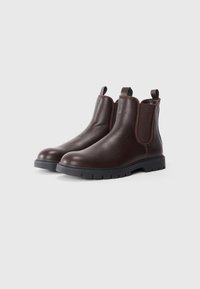 Botas Chelsea de cuero marrón con lados elásticos, punta redonda y suela de goma que presenta un acabado texturizado y un detalle de borde en contraste.