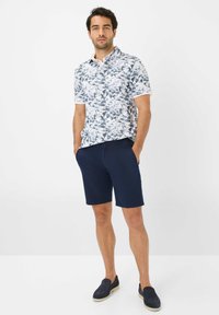 Polo a maniche corte con sfondo bianco e motivo foglia blu, abbinato a pantaloni corti blu navy. Le scarpe sono slip-on blu scuro con suola chiara.