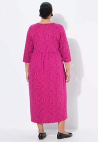 Robe fuchsia à imprimé zèbre, manches trois-quarts, taille cintrée et ourlet droit. Portée avec des ballerines noires.