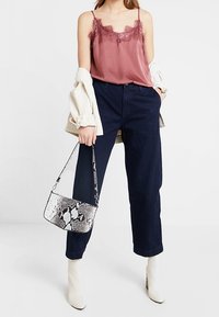 Satin burgunderfarbene Camisole mit Spitze, hoch taillierte dunkle Jeanshose, weiße Knöchelstiefel und eine Handtasche im Schlangenprint.