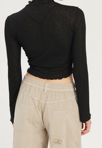 Top nero a maniche lunghe con finitura texturizzata, design cropped e orlo a scallop, abbinato a pantaloni cargo beige con vita elastica e tasche.