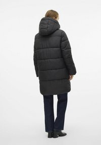 Svart pufferjacka med huva, med ett quiltat mönster och långa ärmar, tillsammans med mörka jeans och ankelstövlar.
