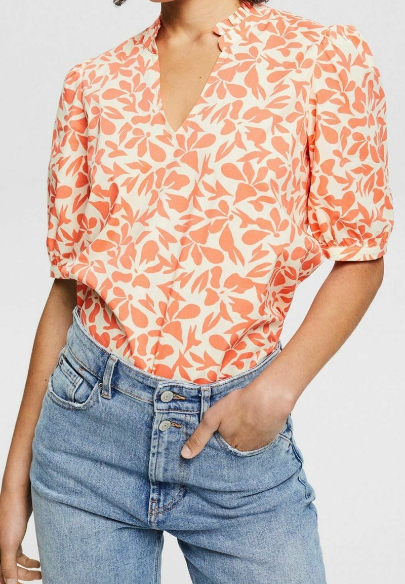 Bluzka z krótkim rękawem z dekoltem w kształcie litery V, wykonana z lekkiego materiału w koralowo-kremowy wzór liści. Połączona z dżinsami w wysokim stanie.