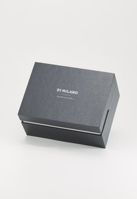 Boîte noire texturée avec une fermeture magnétique, portant "D1 MILANO" et des coordonnées imprimées en blanc sur le dessus. Design simple et élégant.
