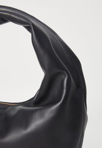 Musta nahkalaukku, jossa on sileä pinta, pyöreä muotoilu ja erottuva taitettu kahva. Varustettu kultaisella vetoketjuyksityiskohdalla.