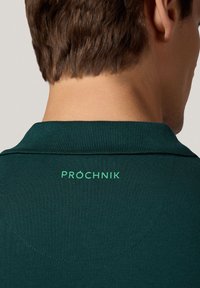 Ciemnozielona koszulka polo z kołnierzykiem, wykonana z teksturowanej tkaniny; logo "PRÓCHNIK" w jasnym zielonym kolorze z tyłu, uzupełniające wzór kołnierza.