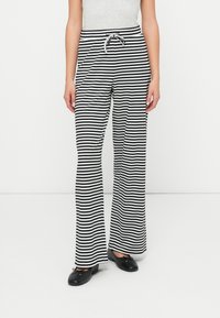 Pantalones de perna larga listrados em preto e branco, com cordão na cintura, feitos de um tecido suave, apresentando um ajuste relaxado e uma silhueta reta.