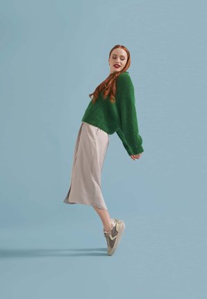 Green knitted sweater, beige satin midi skirt, and gray sneakers. Sweater is oversized with long sleeves; skirt has a side slit and smooth texture.