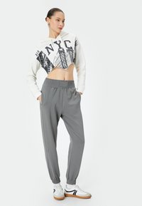 Gekorte witte hoodie met NYC-graphic, gecombineerd met grijze joggers met elastische taille en witte sneakers met zwarte accenten. Glad materialen.