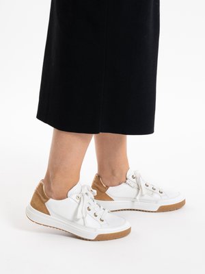 Person wearing black cropped pants and white sneakers with tan accents and laces against a white background.
