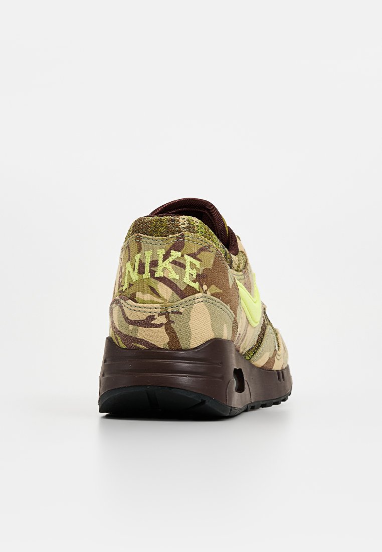 Zapatillas Nike con un patrón de camuflaje en tonos terrosos, acentuadas con un Swoosh y un logo en amarillo brillante, con una suela marrón y un material texturizado.