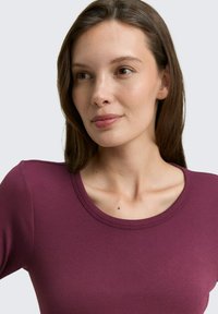 Violet juostelėtas trumpomis rankovėmis marškinėliai su apvalia iškirpte. Audinys atrodo švelnus ir lygus, akcentuojantis dėvėtojo kaklo ir žandikaulio liniją.