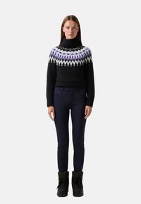 Černý pletený svetr s vysokým límcem, zdobený barevným blokem v purpurové a bílé barvě. V kombinaci s tmavě modrými slim-fit kalhotami a černými botami.