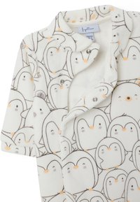 Un body de manga corta hecho de suave tela blanca con un patrón de pingüinos; cuenta con cierres a presión y acentos en un naranja claro.
