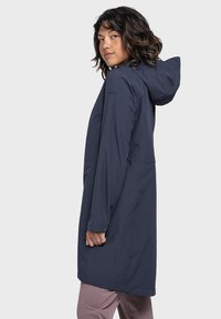 Marineblauer wasserdichter Jacke mit Kapuze, langen Ärmeln und lockerer Passform. Mit einem Logo auf dem Arm und einem Design, das bis zur Mitte des Oberschenkels reicht.