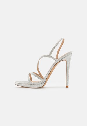 Sandales à talons hauts argentées avec un design à plusieurs lanières, bout carré, matériau texturé, et semelle intérieure beige clair. Hauteur de talon de 10 cm.