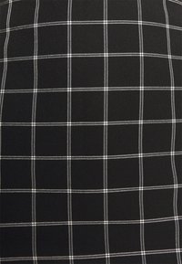 Tissu noir avec un motif de grille blanche composé de lignes verticales et horizontales fines, également espacées, formant des carrés.