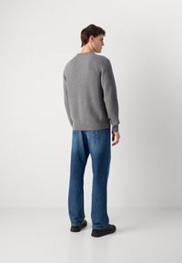 Gray ribbed sweater with a round neck, paired with loose-fitting blue jeans and black shoes, viewed from the back. Simple design, textured fabric.