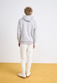 Ljusgrå huvtröja med dragsnodd, mjuk textur och ribbad fåll. Kombineras med vita joggers och vita sneakers med bruna sulor.