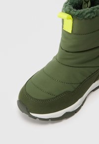 Stivale invernale verde isolato con parte superiore imbottita, foderato in pile, suola bianca e linguetta gialla sul retro.
