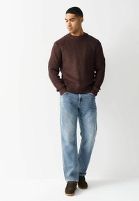 Brūns teksturēts adīts džemperis, gaiši zili taisni džinsi un tumši brūnas kurpes. Vienkāršs dizains ar ribotu piedurkņu un kakla izgriezumu.