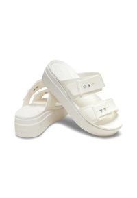 Białe sandały na platformie z dwiema szerokimi paskami i dekoracyjnymi srebrnymi akcentami. Wykonane z miękkiego materiału, z teksturowaną podeszwą i krzyżowym zapięciem.