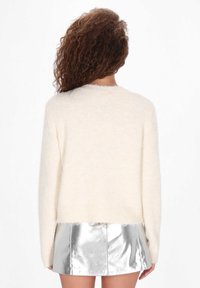 Kremowy, puszysty sweter z okrągłym dekoltem i długimi rękawami, w zestawie z metaliczną srebrną mini spódnicą.