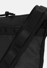 Borsa in tessuto nero con superficie testurizzata, dotata di spallacci regolabili e chiusura a cordoncino. Design minimalista con un focus sull'utilità.