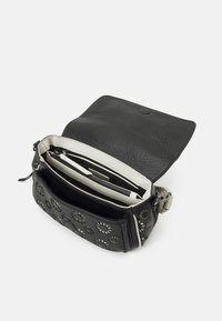 Sac bandoulière noir texturé avec motif floral découpé, rabat ouvert, plusieurs compartiments et doublure intérieure blanche avec poche zippée.
