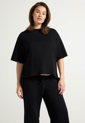 T-shirt oversize in cotone nero con maniche corte, scollatura a girocollo e vestibilità rilassata, abbinata a pantaloni neri con coulisse.