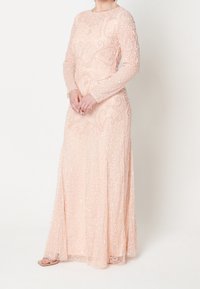 Abito rosa pastello a maniche lunghe con dettagli intricati di perline e paillettes, dotato di corpetto aderente e gonna fluente. Texture liscia ovunque.